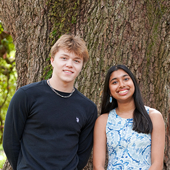 Smiling young man and woman stand together against a large tree trunk.