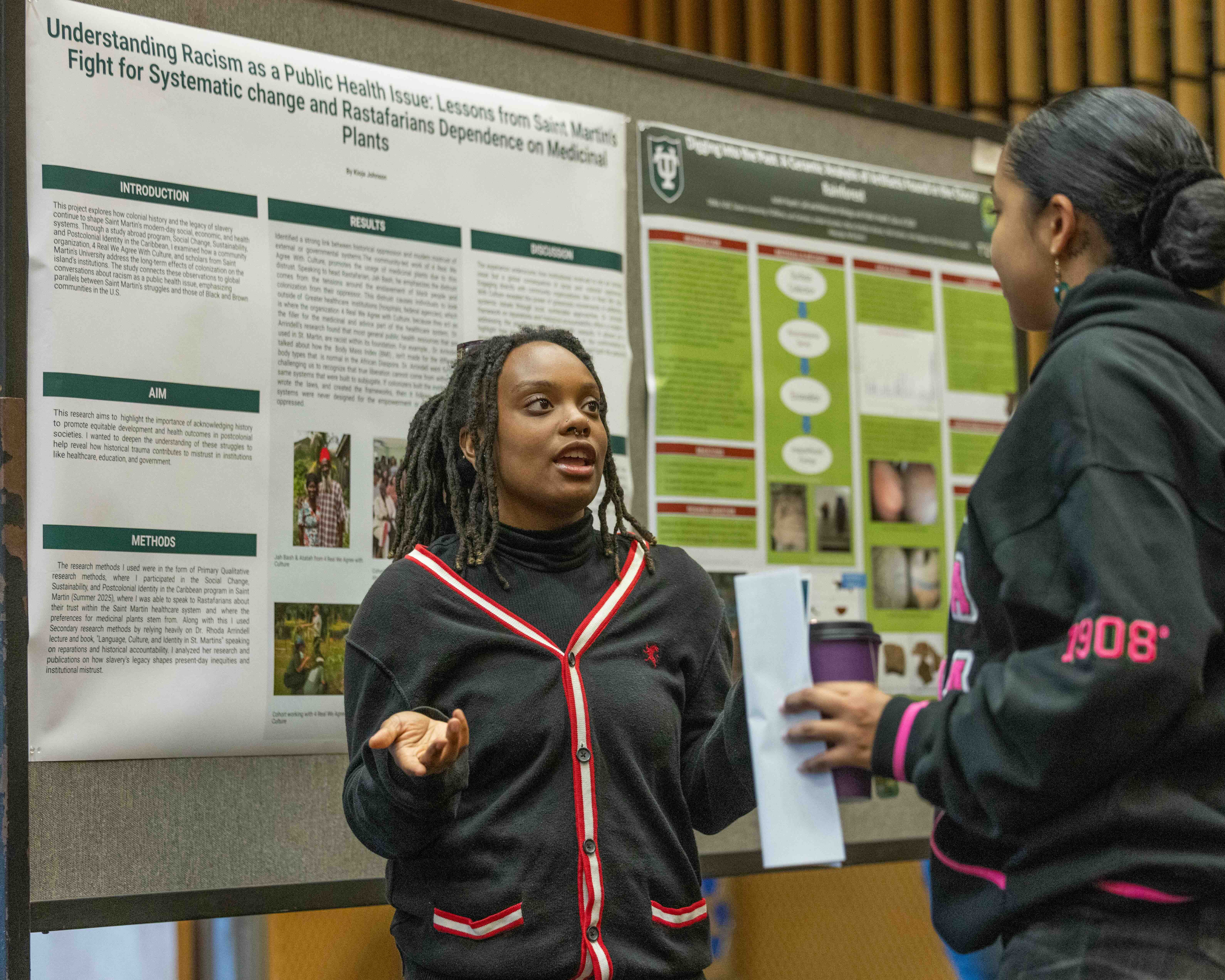 Young woman presents academic poster to another woman holding a cup and papers.