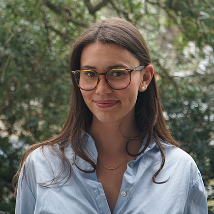 Young woman with long dark hair and glasses wearing a light blue shirt