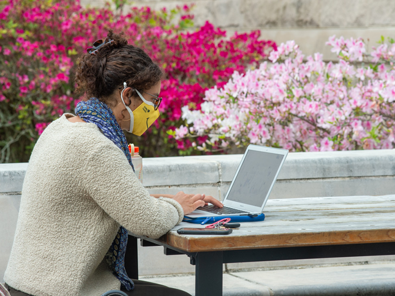 woman sitting outside at picnic table studying with laptop